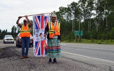 Still strong and dedicated, Elder Angela Ashishkeesh of Attawapiskat First Nation participates in a protest walk against Ontario’s Bill 5 and Canada’s Bill C5. Also seen in the photo is flag bearer Rick Cheechoo, Moose Cree FN.